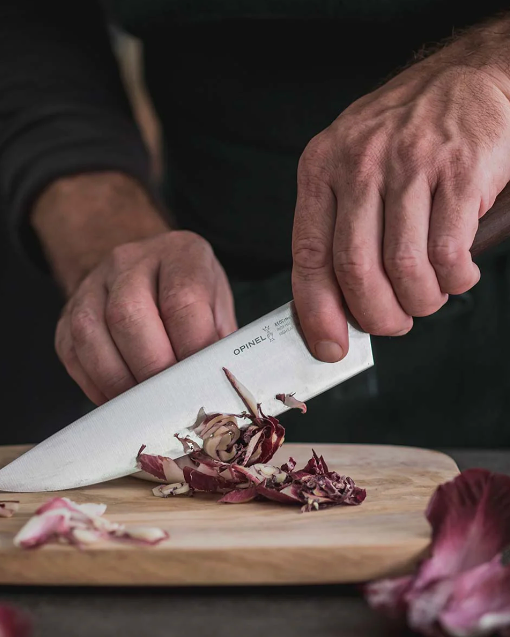 Person using a chef knife on a cutting board with chopped vegetables