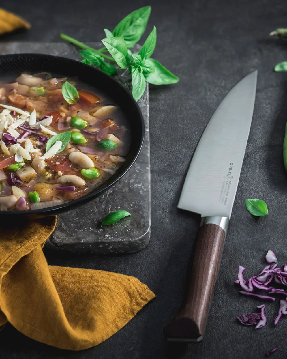 Vegetable stir-fry in a black bowl with a chef's knife and ingredients on a dark surface