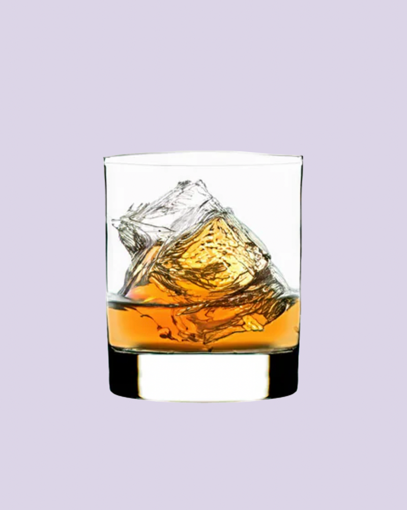 Glass of whiskey with a large ice cube on a light purple background