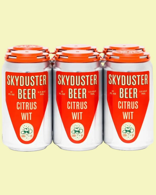 Three white aluminum cans of Skyduster Beer Citrus Wit with bright orange labels and orange lids, arranged side by side on a pale yellow background.